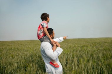 Hintli bir adam oğlunu omuzlarında taşırken bir şeyi işaret ediyor.
