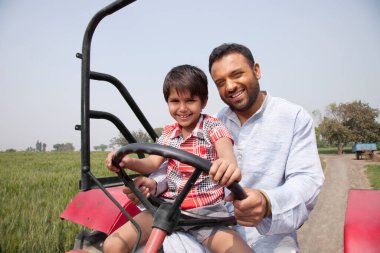 Traktör süren mutlu bir baba oğul portresi.