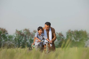 Baba oğluna tarlada bisiklet sürmeyi öğretiyor.