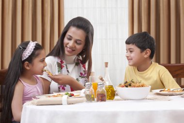 Neşeli anne kızına pizza yedirirken oğlu yanında oturuyordu.