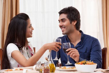 Lokantada birbirlerine bakarken kadeh tokuşturan mutlu genç çift.