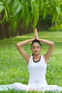 Elleri dua pozisyonunda yoga yapan genç bir kadın.