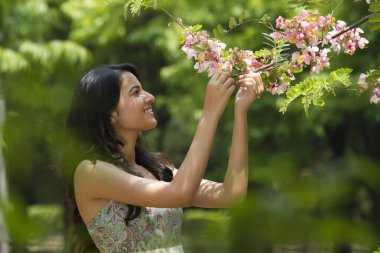 Genç bir kadın daldaki çiçeklere bakıyor.