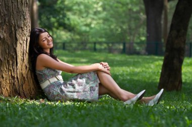 Genç bir kadın ağaca yaslanıyor.