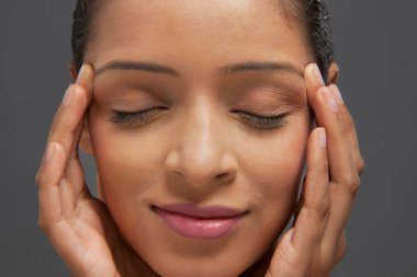 Gözleri kapalı ve parmakları şakaklarda güzel genç bir kadın.