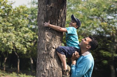 Baba oğlunun ağaca tırmanmasına yardım ediyor.