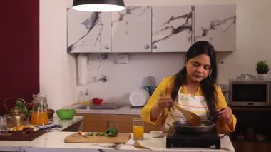 Bir kadın telefonda konuşurken ve yemek pişirirken içkiden zevk alıyor.