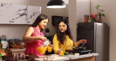 İki kadın dedikodu yaparken yemek pişiriyor ve içkilerinin tadını çıkarıyor.