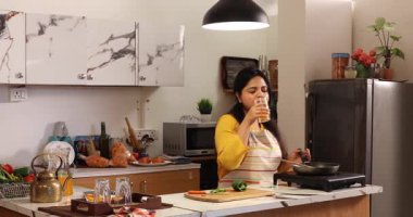 Bir kadın telefonda konuşurken ve yemek pişirirken içkiden zevk alıyor.