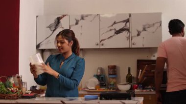 Kadın konteynırda unu kontrol ederken, adam mutfağa cam kase koyuyor.