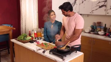 Kadın mutfakta yardım ederken, adam havanda baharat öğütüyor.