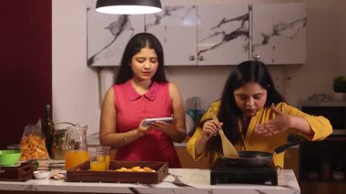 İnternetten yemek tarifi izlerken iki kadın yemek yapıyor.
