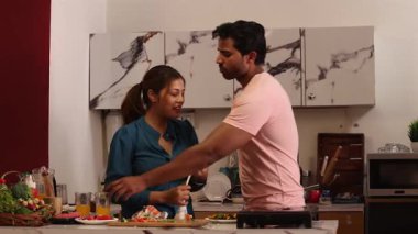 Kadın mutfakta bir şeyler yaparken erkek meyve suyu içiyor.