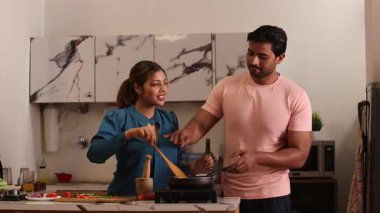 Bir çift mutfakta yemek hazırlarken, bir kadın tavadaki yemeği kokluyor.