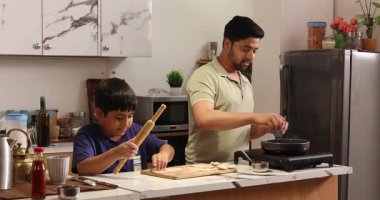 Oğlu mutfakta hamur topluyor ve babası mutfakta chapati yapıyor.