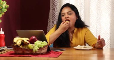 Bir kadın kahvaltı yapıyor ve video görüşmesinde konuşuyor.