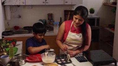 Anne kek hamurunu kek kabına dolduruyor ve oğlu da süslemeye çalışıyor.