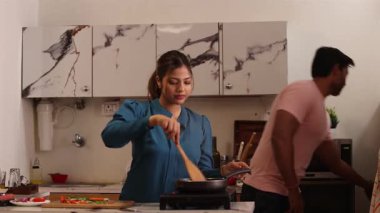 Kadın yemek pişirirken adam önlüğünü değiştirip ona atıştırmalık bir şeyler yediriyordu.