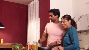 Bir çift mutfakta yemek hazırlarken bir kadın mutfakta meyve suyu içiyor.