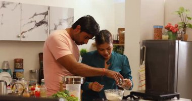 Bir çift mutfakta birlikte yemek pişiriyor ve gülüyor.