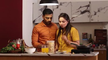 Karı koca mutfakta birlikte yemek pişirirken abur cubur yiyorlar.