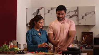 Bir adam havanda baharat öğütüyor ve onları tavaya ekliyor, kadın ise yanında duruyor..