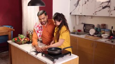 Kocası mutfakta ona yardım ederken mutfak masasını mutfak örtüsüyle silen bir kadın.