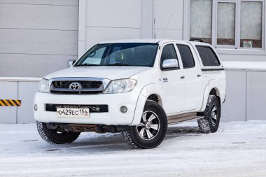 Novosibirsk, Rusya - 02.19.2023: Japon arabasının ön manzarasının yanındaki gri duvarda beyaz renkli Toyota Hilux pikap.