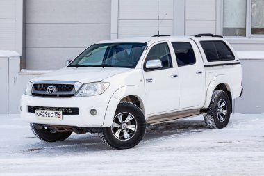 Novosibirsk, Rusya - 02.19.2023: Japon arabasının ön manzarasının yanındaki gri duvarda beyaz renkli Toyota Hilux pikap.