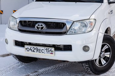 Novosibirsk, Rusya - 02.19.2023: Japon arabasının ön manzarasının yanındaki gri duvarda beyaz renkli Toyota Hilux pikap.