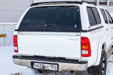 Novosibirsk, Rusya - 02.19.2023: Japon arabasının gri duvar arkası manzarasının yanındaki kar üzerinde beyaz renkli Toyota Hilux pikap.