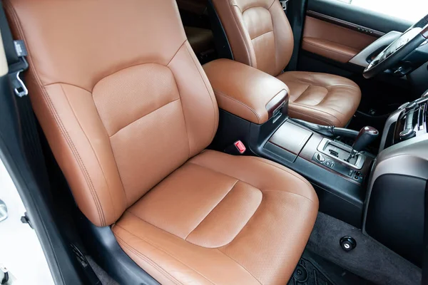 Comfortable front seats inside the car: the driver and passenger, tied with genuine brown leather, modern interior design, the steering wheel covered with brown wood and a luxurious center console.