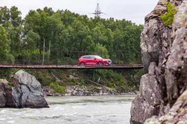 Altai, Rusya - 08. - 20. 2022: Red Haval Jolion arabası kayaların arasındaki nehirden geçen ahşap bir asma köprüye bindi