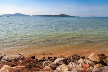 Rawai sahilinden deniz manzaralı, mavi gökyüzünün altında kayalar ve berrak su var.