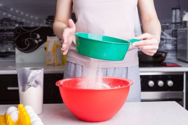 Evde kek yapıyorum. Bir kadın mutfakta paskalya pastası hazırlıyor, eleğe un döküyor..