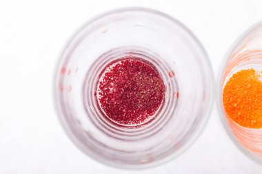 Beyaz bir mutfak masasında şeffaf bardaklar. İçi kırmızı renkte seyreltilmiş gıda boyalarıyla dolu. Paskalya 'dan önce yumurtaları boyamak için hazırlanmış..