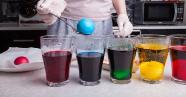 Paskalya için hazırlanırken - mutfak mutfağında renkli yumurtalar lastik eldivenli kadın elleri kaşık kullanarak kaynamış yumurtayı, sulandırılmış mavi boyayla diğer bardakları, daldırılmış yumurtaların farklı renkleriyle temizler..