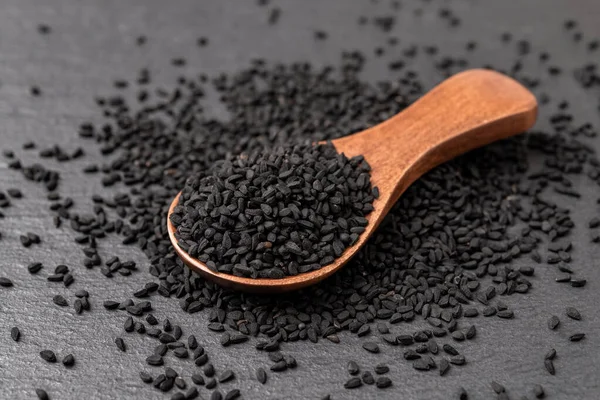 Black cumin seeds in a wooden spoon over black background. Nigella sativa for Ayurveda and herbal medicine and. Kalonji seeds for cooking. Concept of natural spice and seasoning. Macro. Front view.