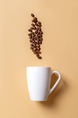 Bej arka planda beyaz kupa ve kavrulmuş kahve çekirdekleri. Kahve içeceği ve sıcak içecek konsepti. Kahvaltı için büyük bir kupa modeli. Modern sofra takımı ve çanak çömlek. Ön görünüm.