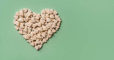Yeşil arka planda kalp şeklinde evcil hayvan besin takviyeleri. Kediler ve köpekler için vejetaryen vitamini. Veteriner doğal hapları konsepti. Evcil hayvanlar için ilaç. Uzayı kopyala Üst görünüm.