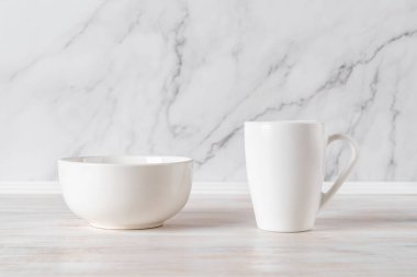 Mermer duvara karşı bir masada kupa ve kupa. Boş ramekin ve yiyecek ve içecek tasarımı için büyük kupa maketi. Modern sofra takımı ve beyaz sofra takımı konsepti. Ön görünüm.