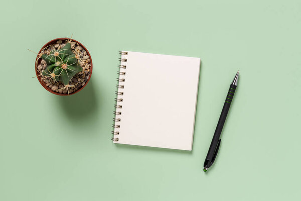 Empty notepad, pen and cactus against green background. Blank notebook for writing day planning, business organizing, life goals. Making to do list mock up. Copy space. Top view.