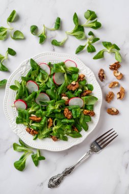 Kuzular marul, turp ve ceviz salatası. Mısır salatası yaprakları, dilimlenmiş turp ve mermer yüzeyde fındık taneleri. Düşük kalorili diyet için vitamin sebze salatası. Dikey çerçeve. Üst görünüm.