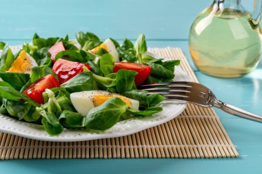 Kuzu salatası, yumurta ve domates salatası. Mısır salatası yaprakları, dörde bölünmüş domates ve turkuaz ahşap bir masada haşlanmış yumurta. Düşük kalorili diyet için vitamin sebze salatası. Ön görünüm.