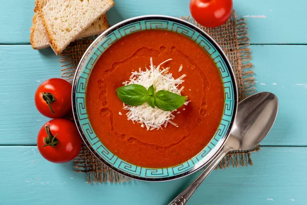 Bowl of homemade tomato soup over turquoise wooden table. Italian hot soup puree of roasted tomatoes with parmesan and basil. Tasty vegetarian dish. Mediterranean cuisine recipe. Top view.