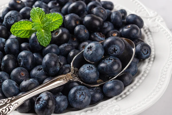 Ripe blueberry on a white plate closeup. Sweet juicy blueberries for vitamin vegan snack and vegetarian dessert. Wild berries as detox diet ingredient. Tasty summer berries. Front view.