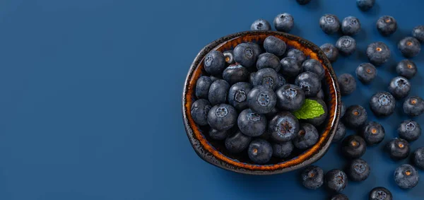 Ripe blueberries in a bowl over blue background. Summer sweet wild berries. Tasty blueberry as vitamin vegetarian dessert and healty vegan snack. Detox diet ingredient. Copy space. Top view.