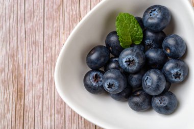 Ahşap yüzey üzerinde beyaz kasede olgun yaban mersini. Vejetaryen vitamini için meyve suyu. Tatlı yabanmersinli vejetaryen tatlı. Detoks diyeti hammaddesi. Yatay çerçeve. Üst görünüm.