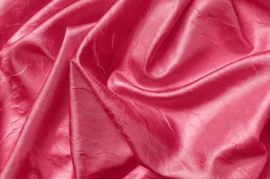 Draped shiny wrinkled silk of viva magenta color texture. Background of folded magenta red satin cloth. Crumpled fabric material design element. Color of the year 2023. Full frame. Top view.