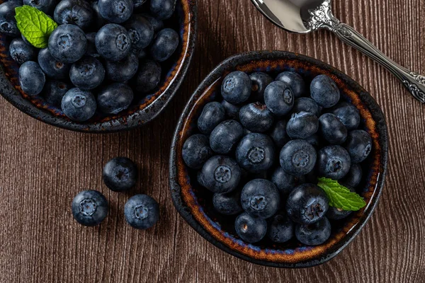 Ripe blueberries in a bowl over wooden background. Ready to eat healthy fruit dessert of wild berries. Tasty fresh blueberry as natural antioxidant. Vegan and vegetarian concept. Top view.